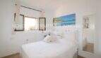 Bright bedroom with double bed, white bedding, wooden windows and ocean view wall picture in Son Servera