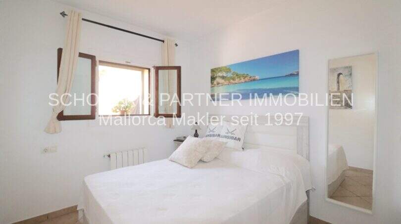 Bright bedroom with double bed, white bedding, wooden windows and ocean view wall picture in Son Servera