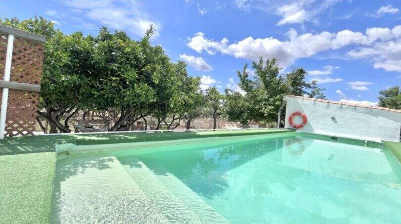 Pool mit türkisem Wasser, Rettungsring und Orangenbäumen der Finca in Campanet unter blauem Himmel.