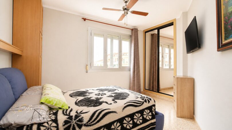 Dormitorio luminoso con cama doble, ventilador de techo, armario espejo y TV en vivienda de playa en Palma