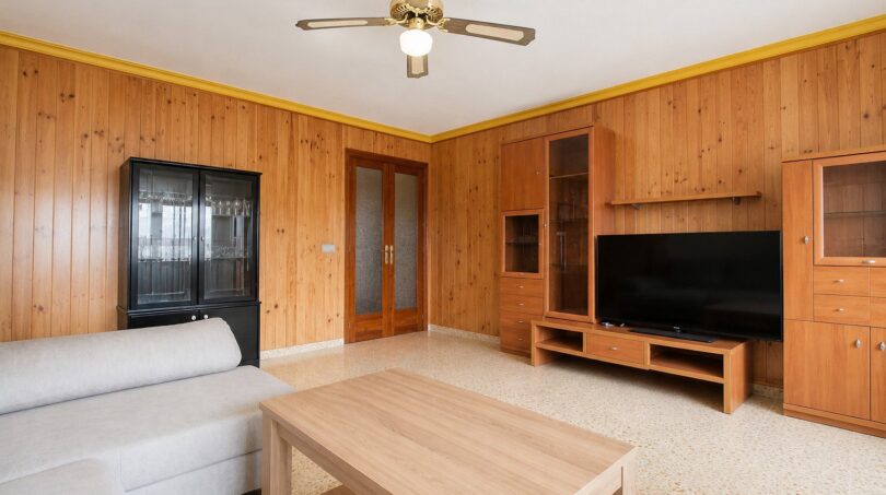 Salón con revestimiento de madera, ventilador de techo, mueble TV y sofá luminoso en Palma de Mallorca