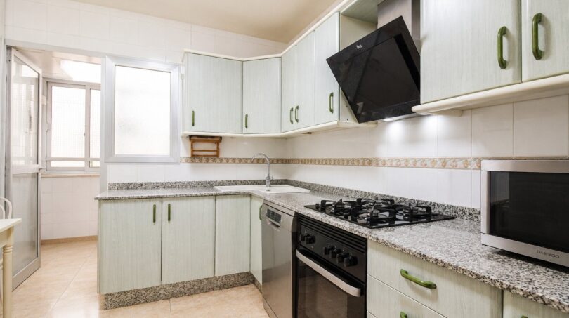 Cocina luminosa con armarios verde menta, encimera de granito, estufa de gas y microondas en vivienda de playa en Palma