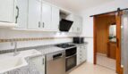 Cocina del apartamento de playa en Palma: encimera de granito, electrodomésticos integrados, armarios blancos, puerta corredera de madera.