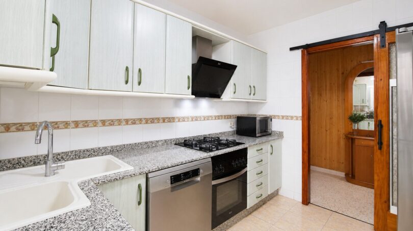 Cocina del apartamento de playa en Palma: encimera de granito, electrodomésticos integrados, armarios blancos, puerta corredera de madera.