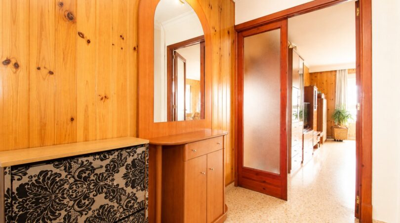 Entrada con revestimiento de madera, espejo, cómoda y puerta corredera en apartamento de playa en Palma de Mallorca