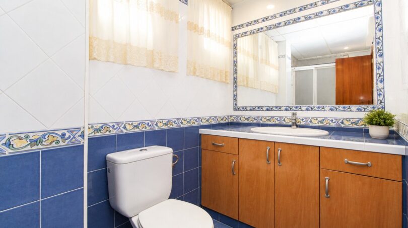 Baño con azulejos azules, mueble inferior de madera, espejo y cenefa decorativa en vivienda de playa en Palma