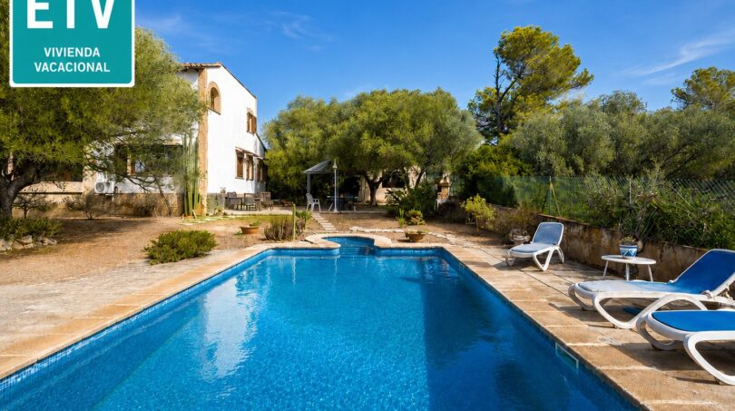 Außenpool mit Liegestühlen, weißer Finca und mediterranem Garten der Ferienvilla in Marratxí