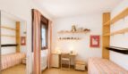 Helles Kinderzimmer mit zwei Betten, Schreibtisch, Holzregalen und rosa Streifenbettwäsche in Palma-Wohnung.