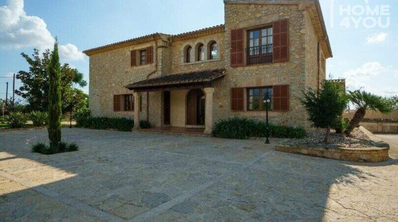 Außenansicht einer mallorquinischen Finca in Lloseta mit Natursteinmauern, braunen Fensterläden und gepflastertem Vorplatz.