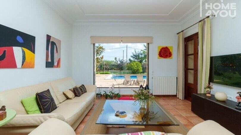 Helles Wohnzimmer der Villa in Lloseta mit Ledersofas, Terrakottaboden und Blick auf den Pool.