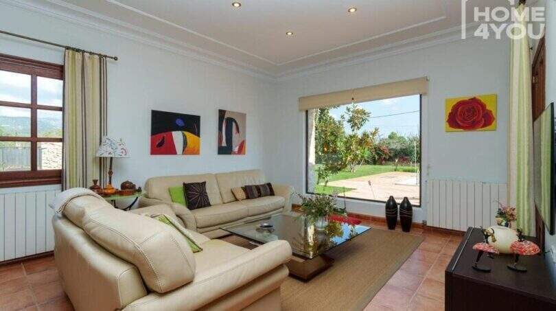Helles Wohnzimmer der mallorquinischen Villa in Lloseta mit Ledersofa, Terrakottaboden und Gartenblick.