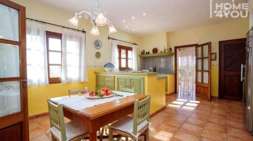 Helle Küche mit Essbereich, grünen Holzmöbeln, gelben Wänden und Terrakottaboden in mallorquinischer Villa, Lloseta.