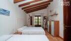Schlafzimmer der mallorquinischen Villa mit zwei Einzelbetten, Holzbalkendecke und rustikalem Terrakottaboden.