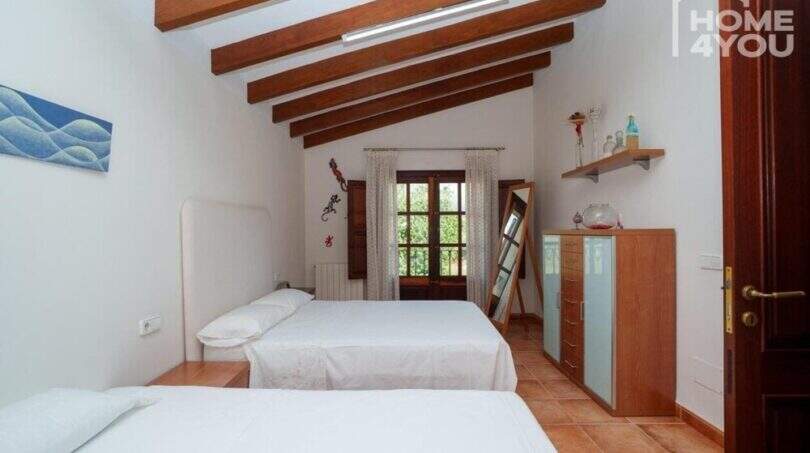 Schlafzimmer der mallorquinischen Villa mit zwei Einzelbetten, Holzbalkendecke und rustikalem Terrakottaboden.