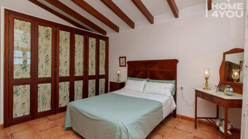 Schlafzimmer der mallorquinischen Villa in Lloseta mit Holzbalkendecke, Doppelbett und rustikalen Einbauschränken.