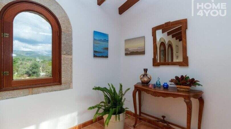Eingangsbereich der mallorquinischen Villa mit Rundbogenfenster, Holzbalken, Konsolentisch und Tramuntana-Blick