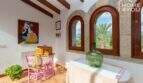 Wohnzimmer der mallorquinischen Villa mit Natursteinbögen, Holzbalken und Blick auf Palmen und Tramuntana-Gebirge.