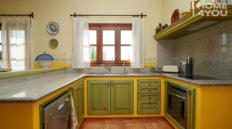 Landhausküche mit grünen Holzfronten, Granitarbeitsplatten und gelbem Wanddesign in mallorquinischer Villa
