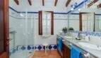 Badezimmer der Villa mit Glasdusche, Doppelwaschbecken, blauen Fliesenakzenten und Holzbalkendecke