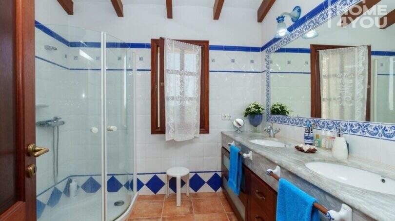 Badezimmer der Villa mit Glasdusche, Doppelwaschbecken, blauen Fliesenakzenten und Holzbalkendecke