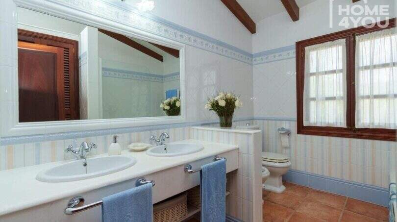 Helles Badezimmer der Villa in Lloseta mit Doppelwaschbecken, Holzbalkendecke und blau-weißen Fliesen.