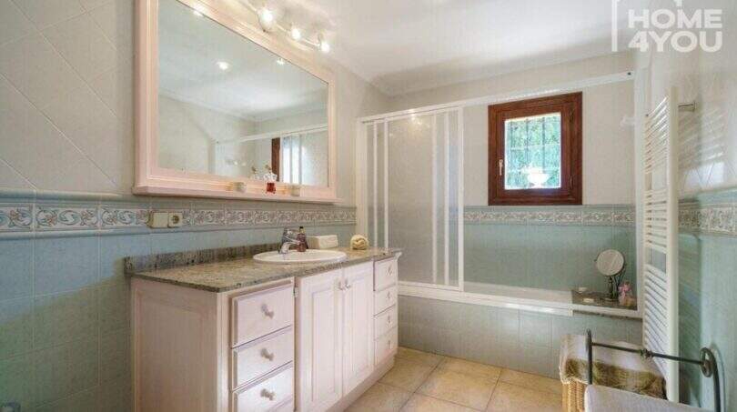 Baño luminoso de la finca con bañera, ducha, lavamanos de granito y bordes decorativos de azulejos.