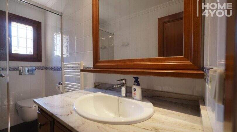 Elegante baño de la finca con tocador de mármol, espejo de madera, ducha y radiador.