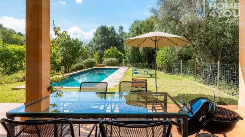 Überdachte Terrasse mit Glastisch, Blick auf Pool und Garten der mediterranen Finca in Campanet