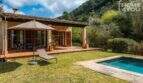 Finca Campanet: Terrasse mit Holzverkleidung, Liegestuhl, Sonnenschirm und kleinem Pool vor bewaldeter Bergkulisse.