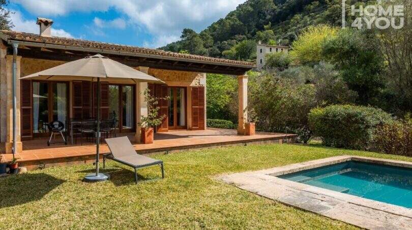Finca Campanet: Terrasse mit Holzverkleidung, Liegestuhl, Sonnenschirm und kleinem Pool vor bewaldeter Bergkulisse.
