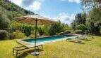 Sonniger Pool mit Liegestühlen und Sonnenschirm, umgeben von mediterranem Grün auf der Finca in Campanet.