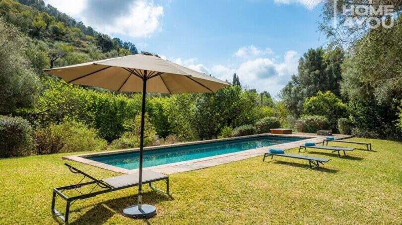 Sonniger Pool mit Liegestühlen und Sonnenschirm, umgeben von mediterranem Grün auf der Finca in Campanet.