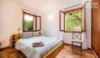 Helles Schlafzimmer der Finca Campanet mit Doppelbett, Holzrahmen-Fenstern und Blick ins Grüne.