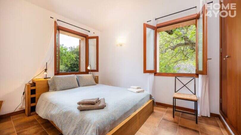 Helles Schlafzimmer der Finca Campanet mit Doppelbett, Holzrahmen-Fenstern und Blick ins Grüne.