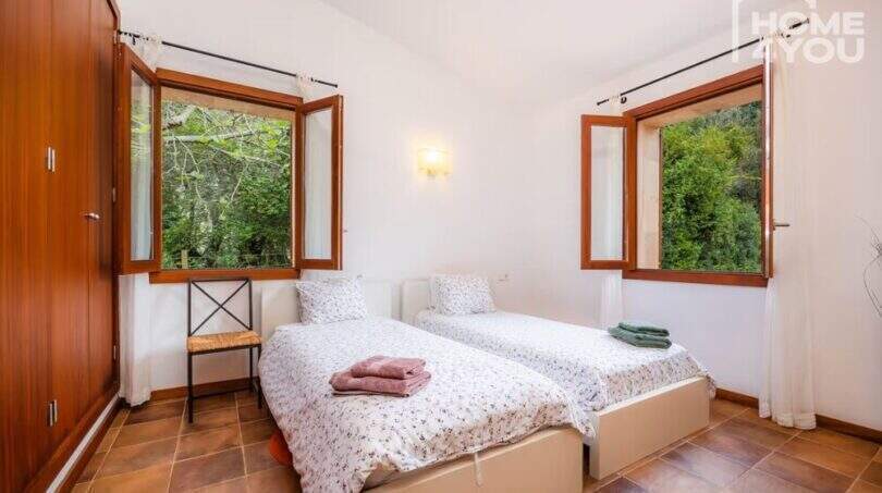Helles Schlafzimmer der Finca in Campanet mit zwei Einzelbetten, Holzschränken und zwei Fenstern mit Naturblick.