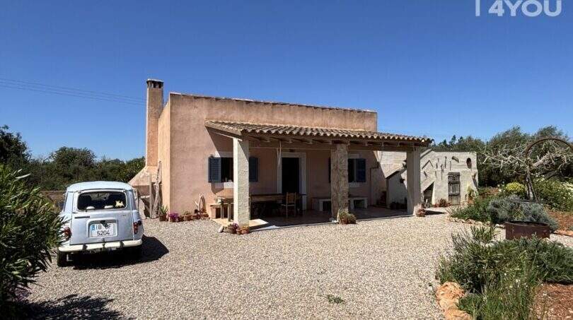 Exterior view of Finca Felanitx: Mediterranean country house with terrace, fireplace, natural stone garden and classic vintage car on gravel driveway.