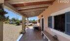 Covered terrace of the finca near Felanitx with wooden beam ceiling, natural stone pillars and view of gravel driveway.