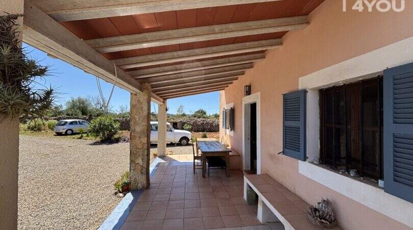 Covered terrace of the finca near Felanitx with wooden beam ceiling, natural stone pillars and view of gravel driveway.