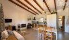 Open living-dining area with wooden beam ceiling, fireplace, built-in kitchen and rustic charm of the finca near Felanitx