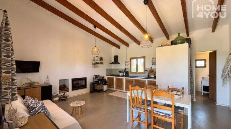 Open living-dining area with wooden beam ceiling, fireplace, built-in kitchen and rustic charm of the finca near Felanitx