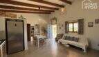 Open living-kitchen area of the finca with wooden beam ceiling, stainless steel refrigerator and blue entrance door