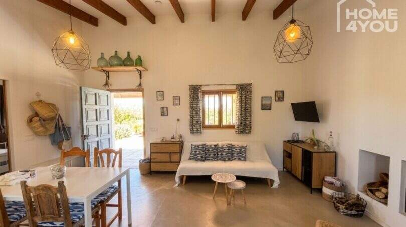 Living area of Finca Felanitx with wooden beam ceiling, fireplace, dining table and lounge area with TV