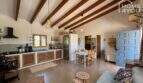 Rustic living room with open kitchen, wooden beam ceiling, dining table and blue entrance door of the finca near Felanitx