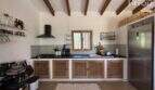 Rustic kitchen of Finca Felanitx with wooden beam ceiling, natural wood cabinets, black worktop and stainless steel refrigerator