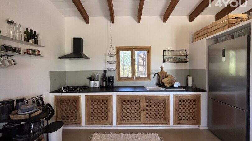Rustic kitchen of Finca Felanitx with wooden beam ceiling, natural wood cabinets, black worktop and stainless steel refrigerator