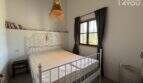 Bedroom of Finca Felanitx with white metal bed, rattan lamp, bookshelf and window with dark curtains.