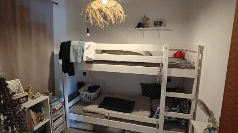 Children's room with white bunk bed, wooden beam ceiling, pendant light and bookshelf in finca near Felanitx