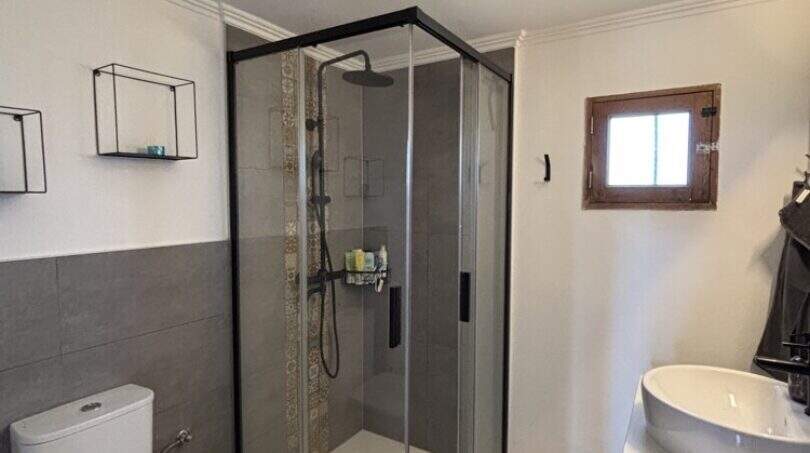 Modern bathroom of Finca Felanitx with glass shower, toilet and sink, gray tile accents.
