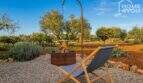 Garden area of Finca Felanitx with fireplace, sun lounger and olive trees under blue sky.