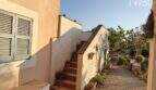 Outdoor area of Finca Felanitx: Terrace with stairs, potted plants, wooden window shutters and Mediterranean garden with cacti.